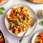 A plate of tofu scramble next to a pan of tofu scramble and a tray of bread.