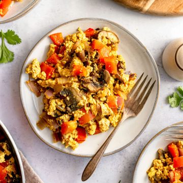 A plate of tofu scramble next to a pan of tofu scramble and a tray of bread.