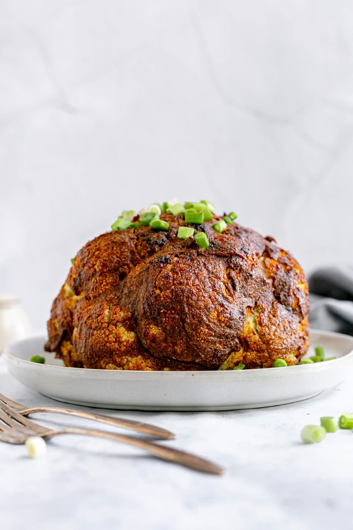 A fried cauliflower on a platter, garnished with scallions.