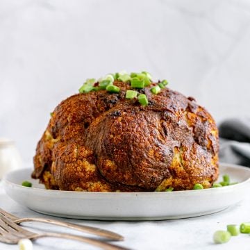 A fried cauliflower on a platter, garnished with scallions.