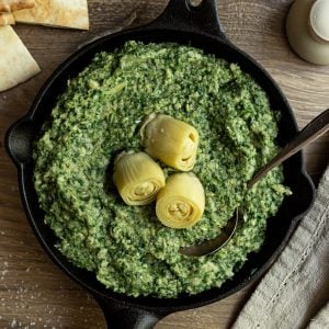A cast iron pan filled with spinach artichoke dip, topped with artichokes.