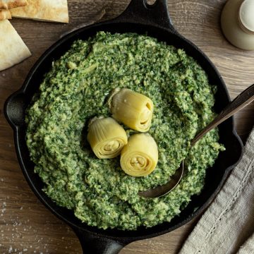 A cast iron pan filled with spinach artichoke dip, topped with artichokes.