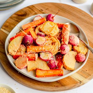 A plate of sesame mustard glazed vegetables, with a spoon, ready to serve.