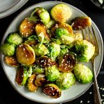 A plate of skillet fried brussels sprouts, garnished with sesame seeds.