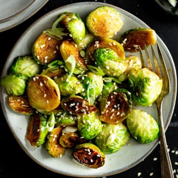 A plate of skillet fried brussels sprouts, garnished with sesame seeds.