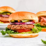 Several black bean burgers on a countertop, with toppings and buns.