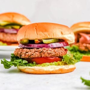 Several black bean burgers on a countertop, with toppings and buns.