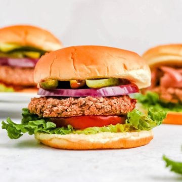 Several black bean burgers on a countertop, with toppings and buns.