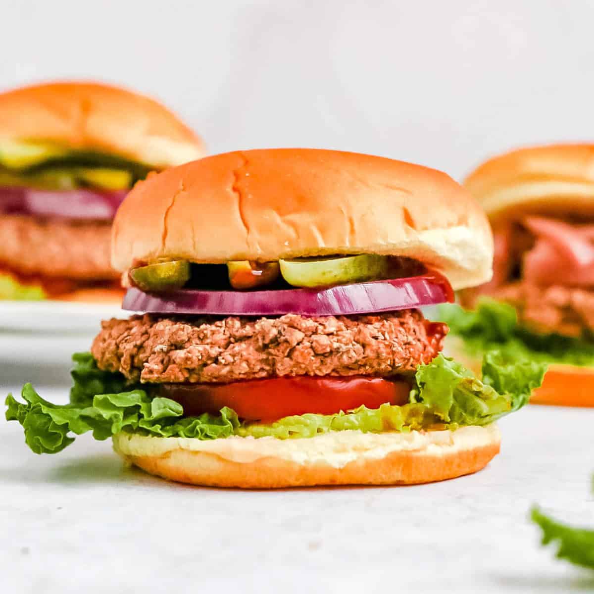 Several black bean burgers on a countertop, with toppings and buns.