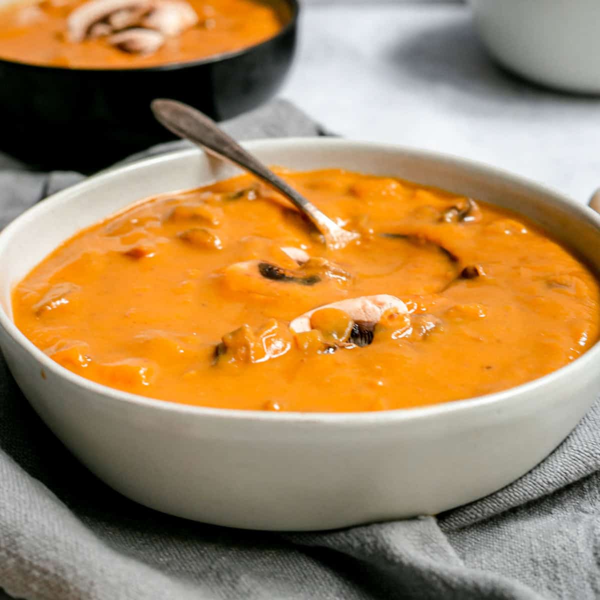 A bowl of sweet potato miso mushroom soup, with a spoon, ready to serve.
