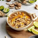 A bowl of Thai-style jackfruit coconut soup, on a platter, with limes, ready to serve.