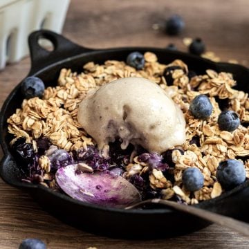 A spoon in a pan of blueberry crumble.