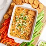 A dish of Vegan Buffalo Chicken Dip on a tray of crackers, carrot sticks, and celery.