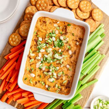 A dish of Vegan Buffalo Chicken Dip on a tray of crackers, carrot sticks, and celery.