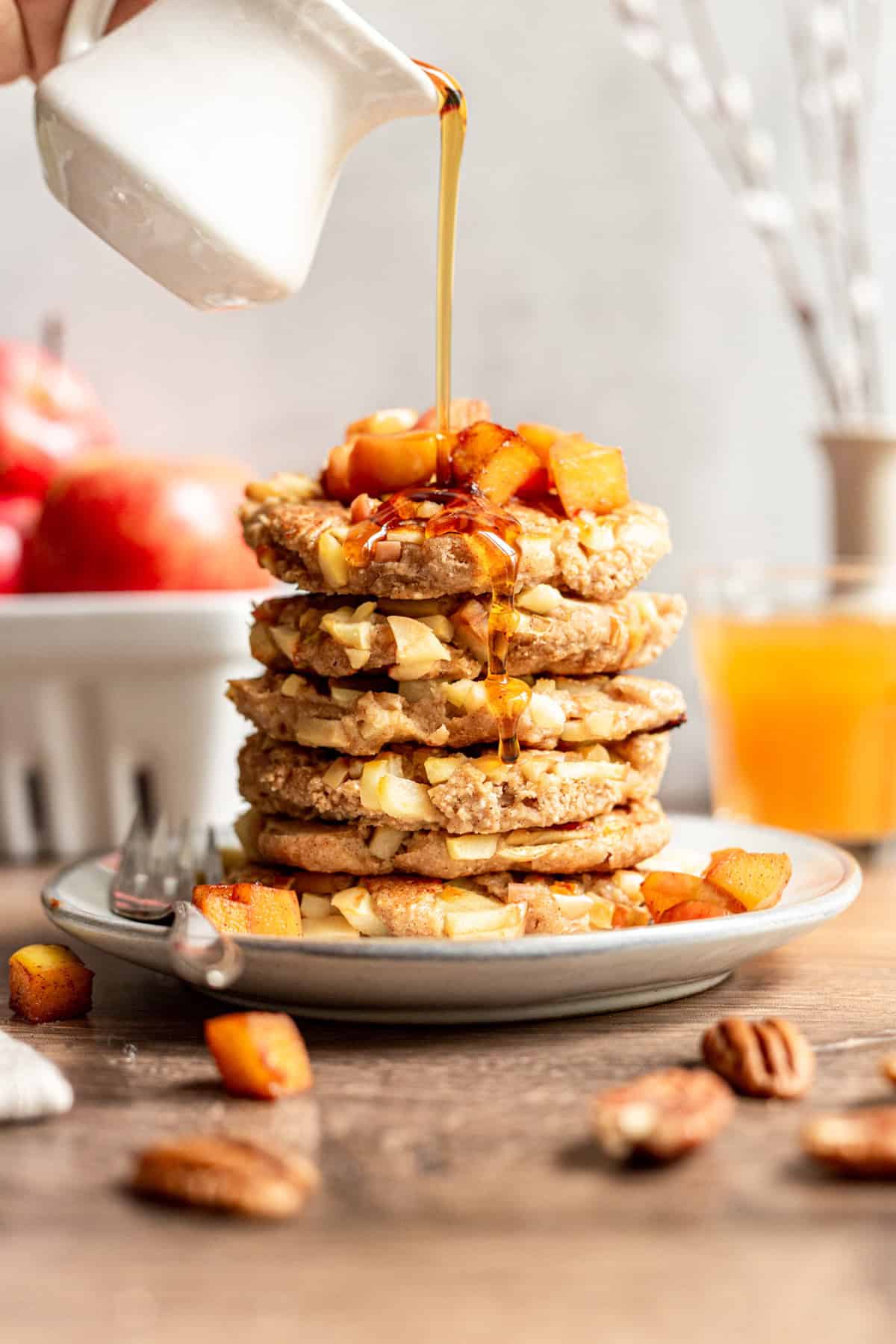 A stack of vegan German apple pancakes being drizzled with maple syrup.