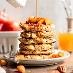 A stack of vegan German apple pancakes being drizzled with maple syrup.