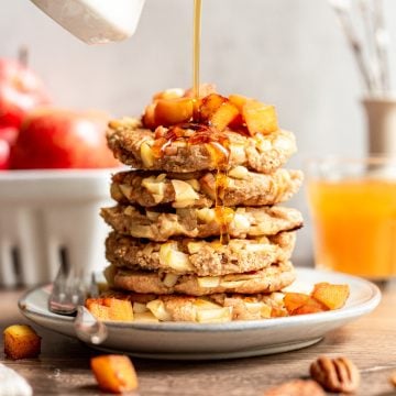 A stack of vegan German apple pancakes being drizzled with maple syrup.