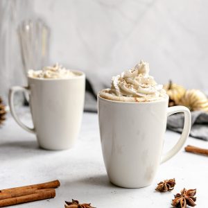 Two mugs of vegan snickerdoodle latte, topped with whipped cream.