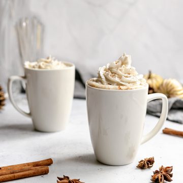 Two mugs of vegan snickerdoodle latte, topped with whipped cream.
