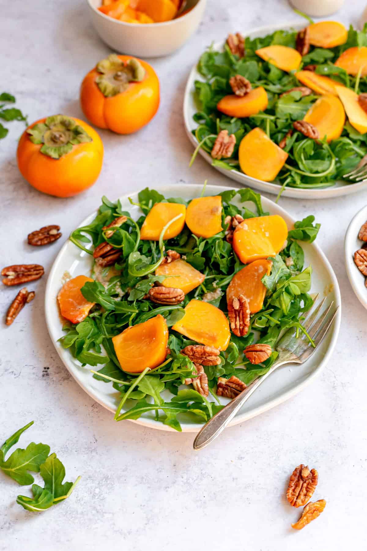 A plate of arugula persimmon salad, with a fork, ready to serve.