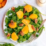 A plate of arugula persimmon salad, with a fork, ready to serve.