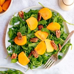 A plate of arugula persimmon salad, with a fork, ready to serve.