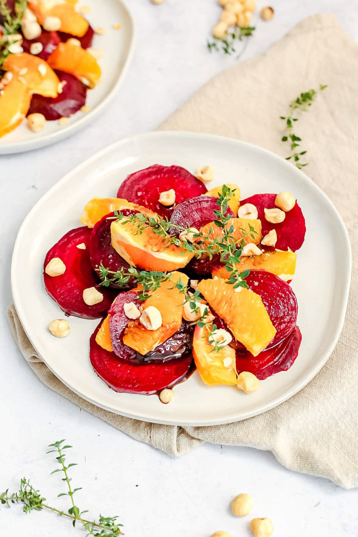 A plate of balsamic beet orange salad, topped with sprigs of fresh thyme.