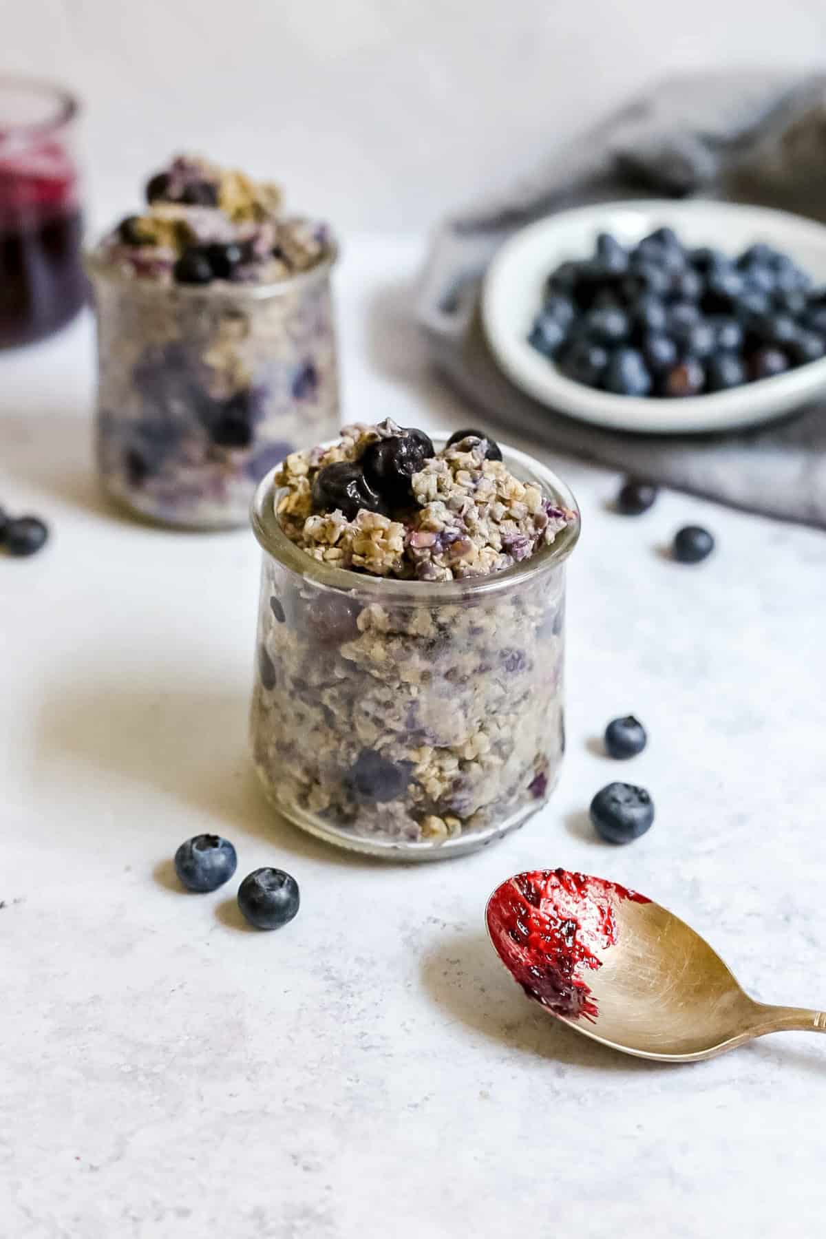 A jar of blueberry maple overnight oats, with a spoon covered in blueberry jam.