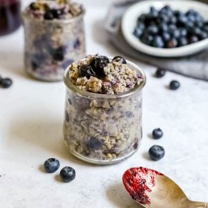 A jar of blueberry maple overnight oats, with a spoon covered in blueberry jam.