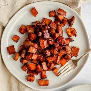 A plate of bourbon glazed sweet potatoes, with a fork, ready to serve.