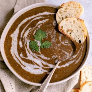 A bowl of cilantro lemon black bean soup, garnished with cilantro and two slices of french bread.