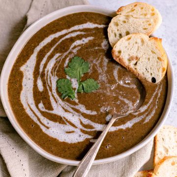 A bowl of cilantro lemon black bean soup, garnished with cilantro and two slices of french bread.
