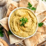 A bowl of coconut curry hummus on a plate of pita.