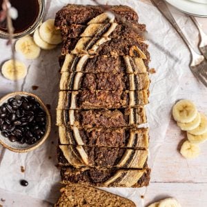 A loaf of coffee banana bread, sliced, with banana slices and coffee beans.