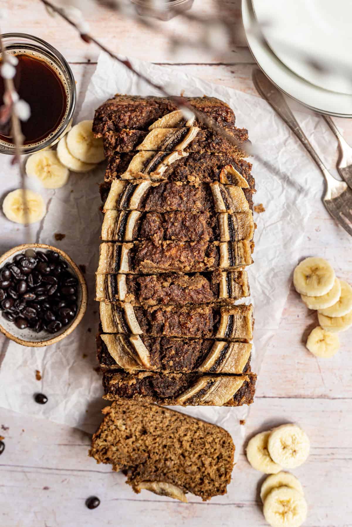 A loaf of coffee banana bread, sliced, with banana slices and coffee beans.