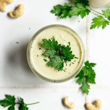 A mason jar of garlic parsley aioli, topped with a parsley leaf.
