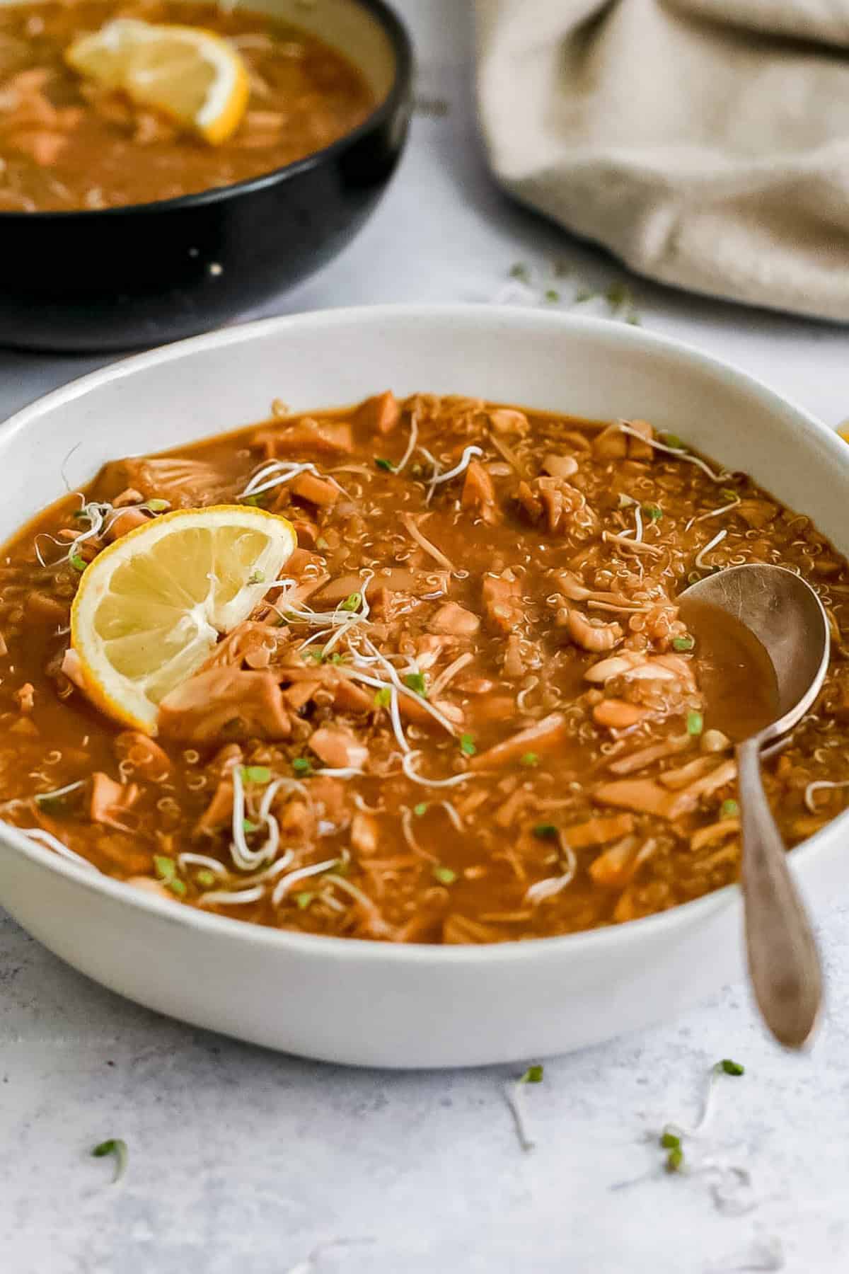 A bowl of jackfruit lemon quinoa soup, garnished with a lemon wedge.