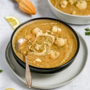 A bowl of lemon mustard cauliflower soup with a spoon, ready to serve.