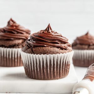 A freshly frosted cupcake on the counter, with a piping bag next to it.
