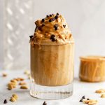 A glass filled with peanut butter protein nice cream, topped with peanut butter and chocolate chips.