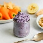 A jar of purple cabbage hummus with a plate of vegetables.