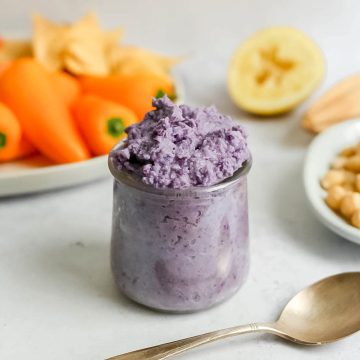 A jar of purple cabbage hummus with a plate of vegetables.