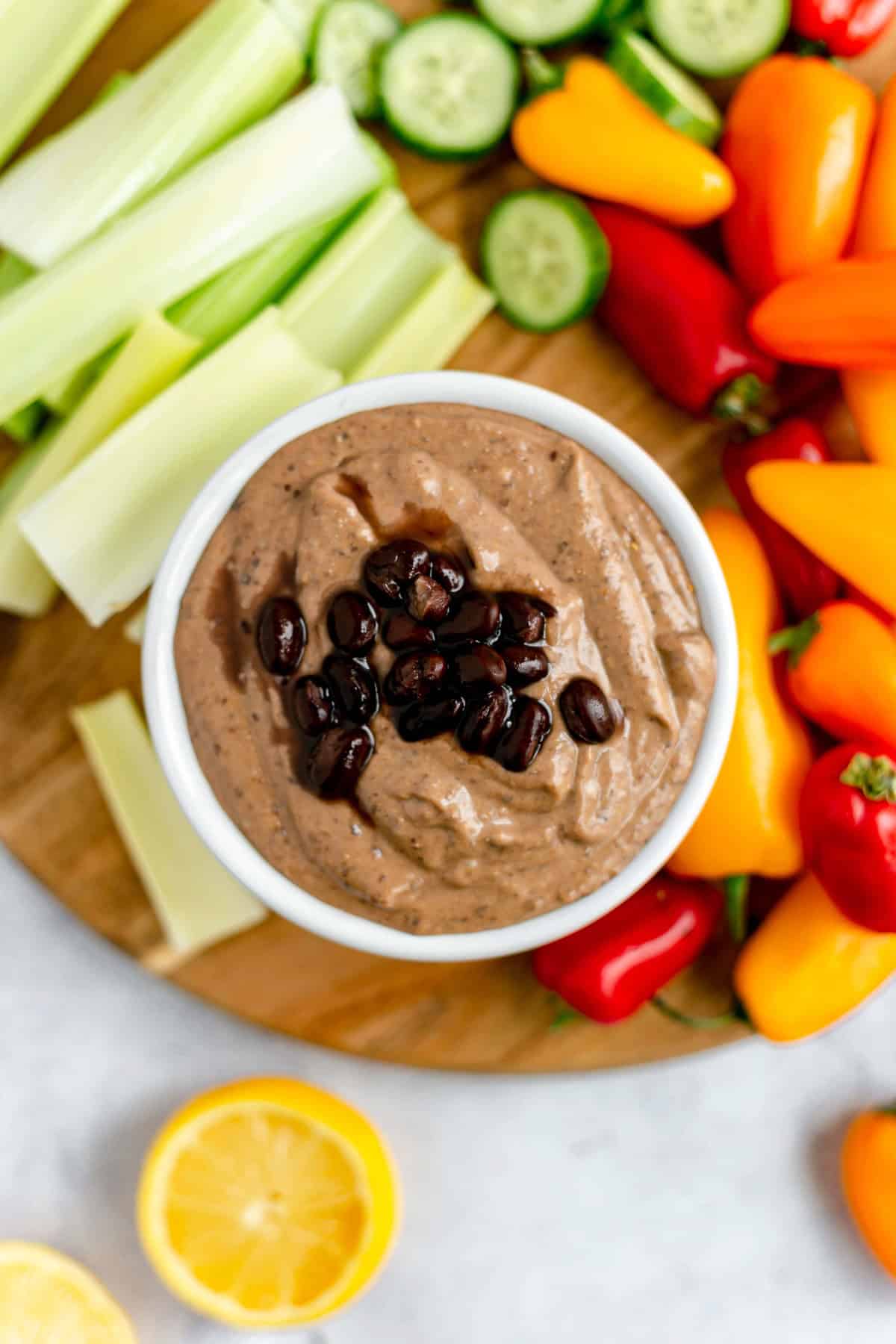 A bowl of smoky black bean dip, topped with black beans, on a tray of fresh vegetables.