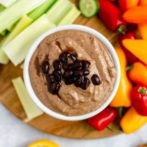 A bowl of smoky black bean dip, topped with black beans, on a tray of fresh vegetables.