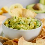 A bowl of spicy corn guacamole with two chips dipped in.