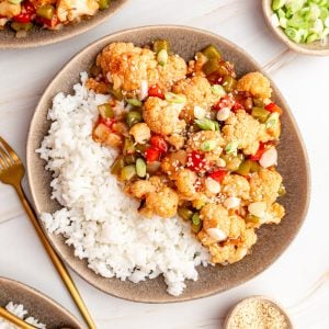 A plate of rice and sweet and sour cauliflower, garnished with sesame seeds and scallions.