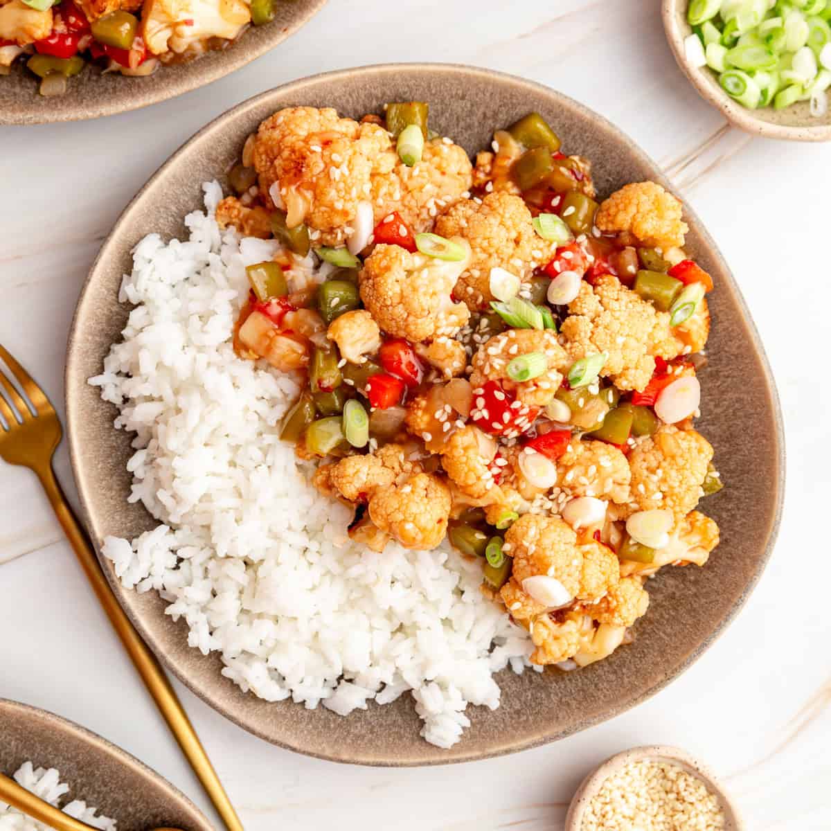A plate of rice and sweet and sour cauliflower, garnished with sesame seeds and scallions.