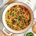 A pot of freshly cooked vegan chicken noodle soup, with bowls and spoons surrounding it.