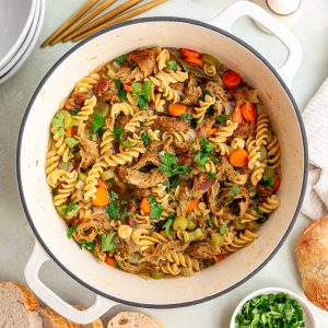 A pot of freshly cooked vegan chicken noodle soup, with bowls and spoons surrounding it.