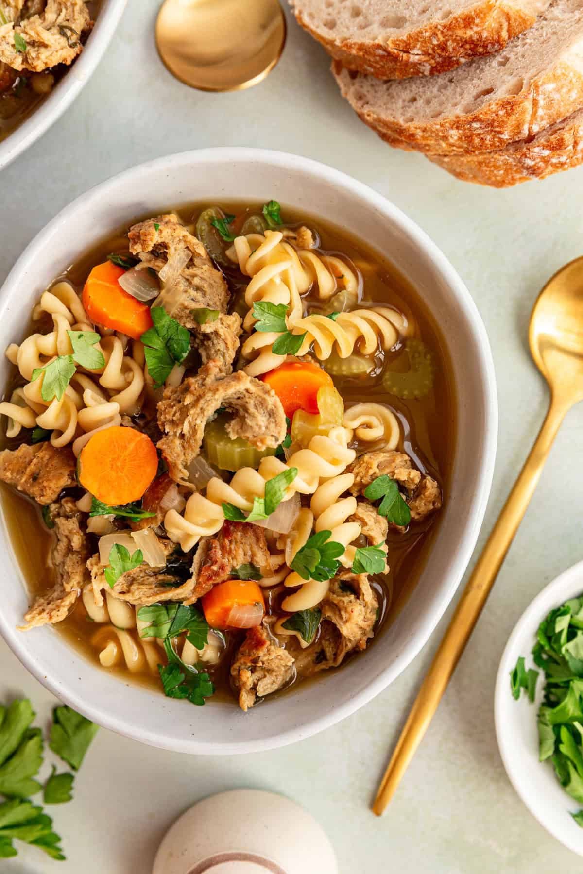 A bowl of vegan chicken noodle soup, with a spoon and some bread, ready to serve.